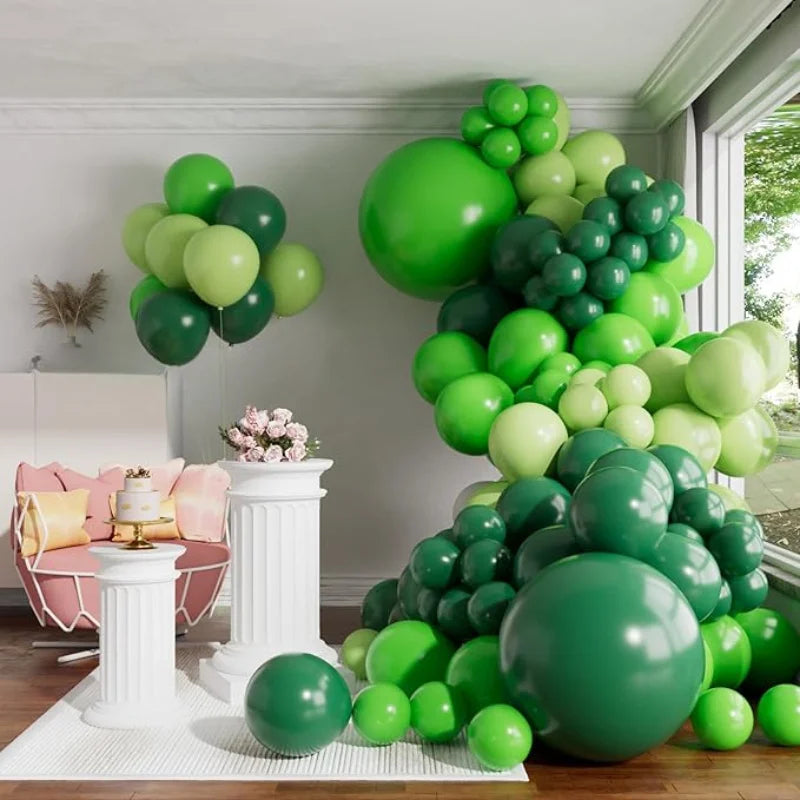 A large green balloon garland arch display featuring various shades of green balloons in a room setting.