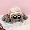 A soft, gray plush toy of Lucas the Spider with large black eyes is displayed on a white box.