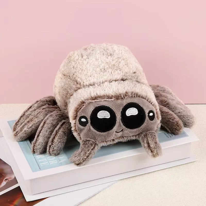 A soft, gray plush toy of Lucas the Spider with large black eyes is displayed on a white box.