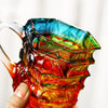 A hand-painted orange glass mug with a green design is held by a person.