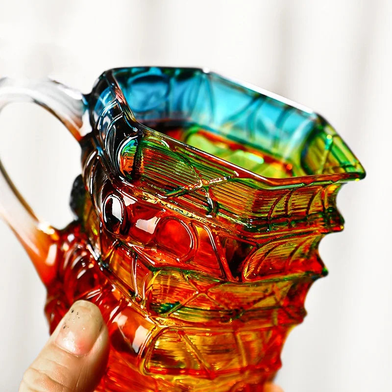 A hand-painted orange glass mug with a green design is held by a person.