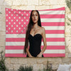 A woman wearing a black strapless dress stands in front of an American flag tapestry featuring red, white, and pink stripes a