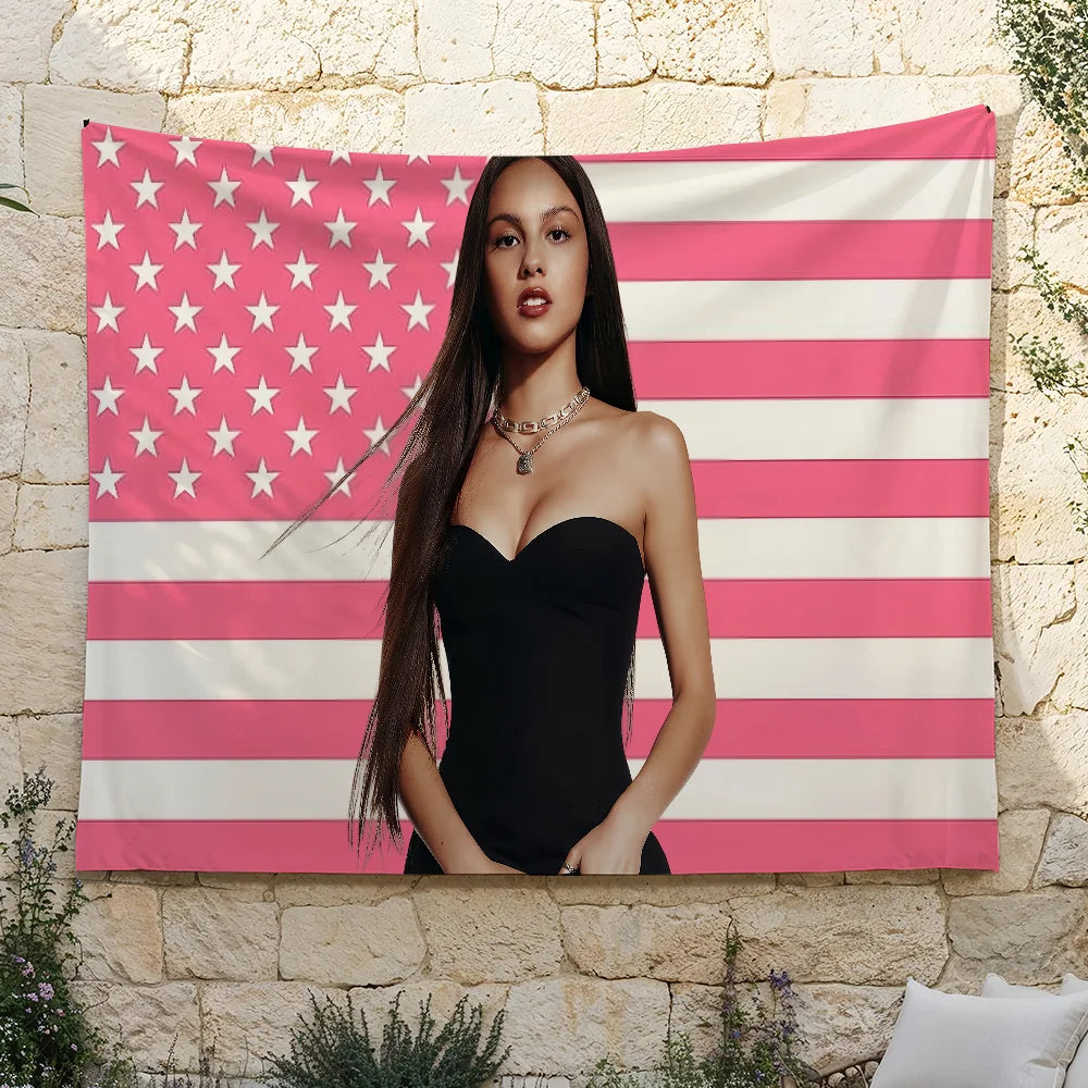 A woman wearing a black strapless dress stands in front of an American flag tapestry featuring red, white, and pink stripes a