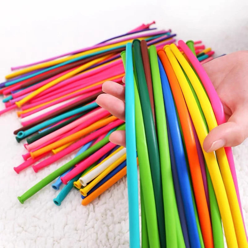 A hand holds a bundle of assorted latex balloons in various bright colors like pink, yellow, green, and orange.