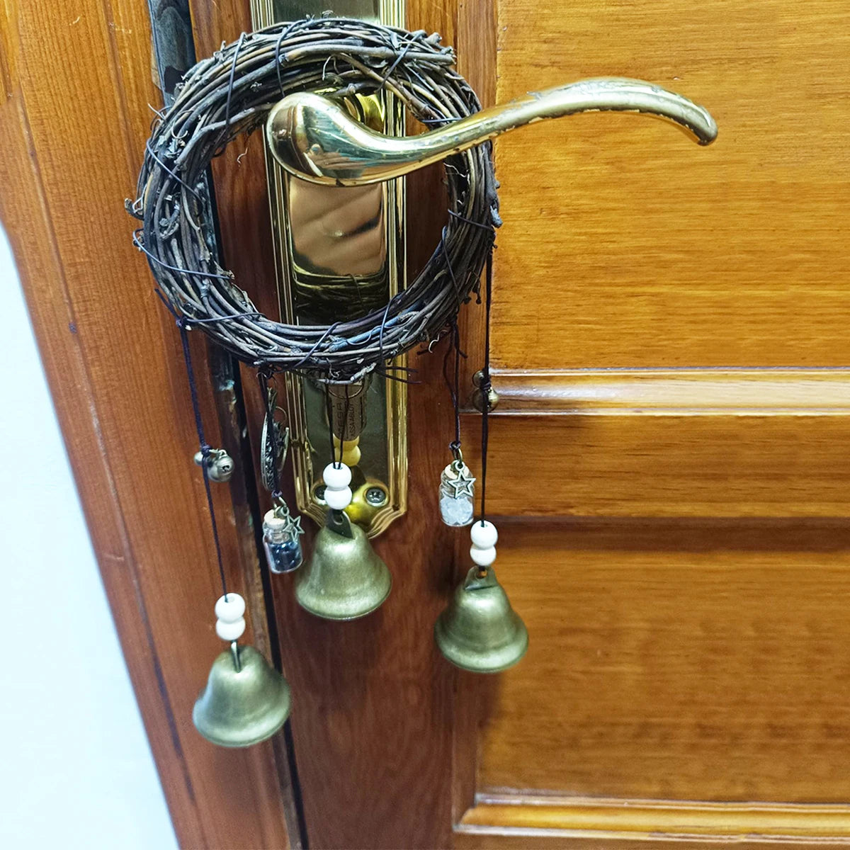 A vintage wicker key bell with a brass handle and multiple hanging bells mounted on a wooden door.