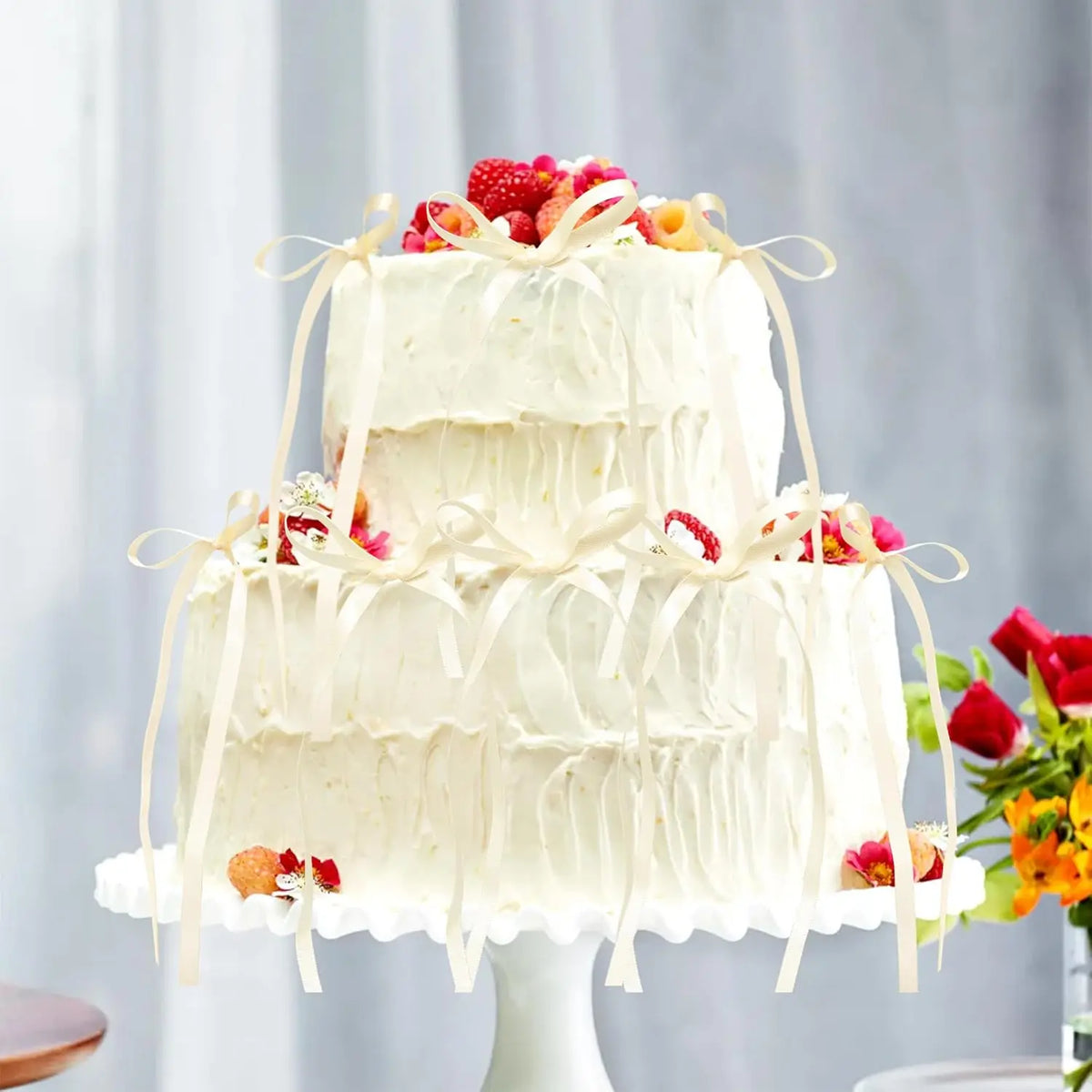 A two-tiered white cake decorated with pink and red fruit and elegant ribbon bows.