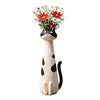 A whimsical resin cat figurine with a black and white coat holding a bouquet of red and yellow flowers.