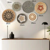 A collection of round boho straw wall hangings in various sizes and textures displayed on a light gray wall above a wooden ca