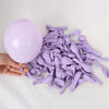 A hand holds a large purple latex balloon next to a pile of 50-piece latex balloon party set in macaron, metallic & confetti 