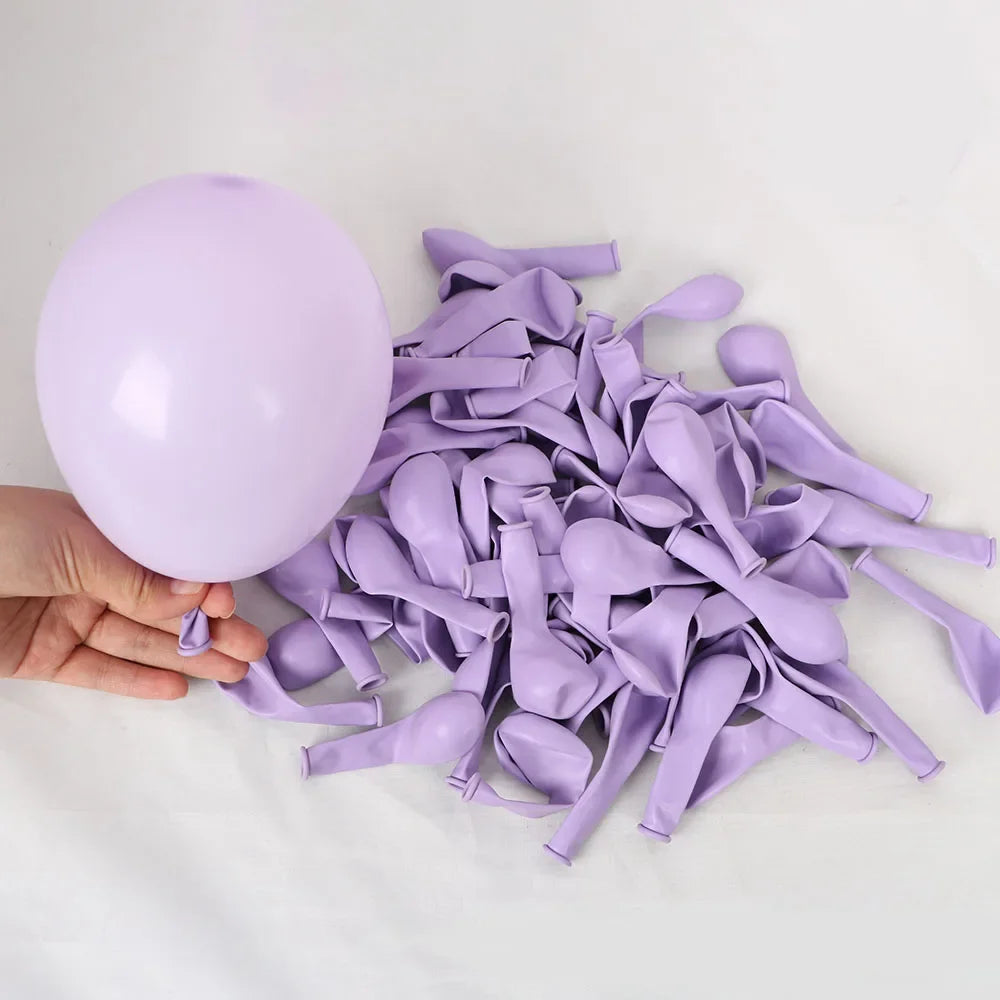 A hand holds a large purple latex balloon next to a pile of 50-piece latex balloon party set in macaron, metallic & confetti 