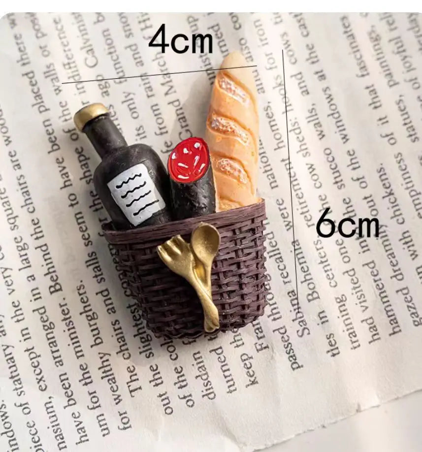 A set of three 3D fruit fridge magnets featuring a banana, avocado, and a slice of orange on a woven basket.