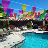 Colorful pennant banner flags strung across a backyard patio and pool area on a sunny day.