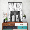 Black and white photograph of the Brooklyn Bridge framed in a black canvas print displayed on a wooden cabinet.