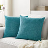 A set of two teal linen pillows resting on a white sofa with a cream knitted blanket.