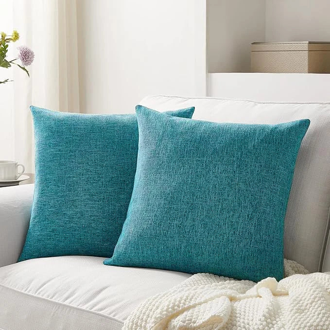 A set of two teal linen pillows resting on a white sofa with a cream knitted blanket.