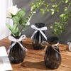 Three faceted diamond crystal vases with natural greenery and white ribbon on a wooden table.