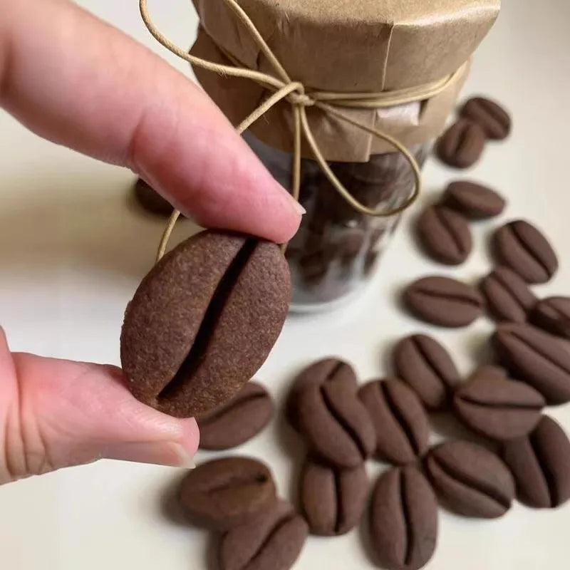 A hand is pressing a dark brown coffee bean cookie stamp mold into a jar of coffee beans.