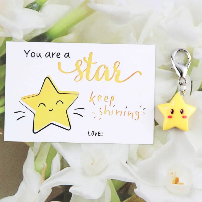 A card with the text You are a star keep shining and a yellow star keychain hanging from a silver ring surrounded by white fl