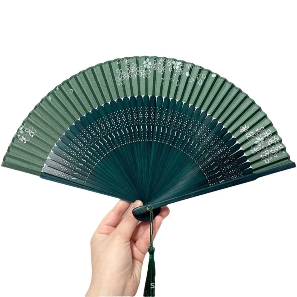 Elegant bamboo folding fan in dark green with a classic design being held by a hand.