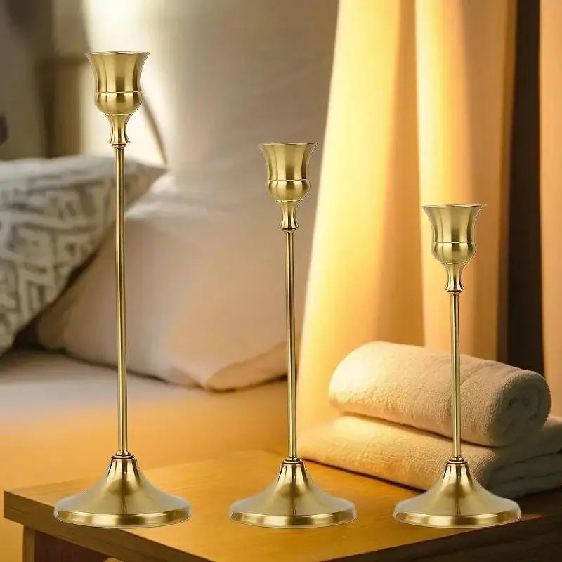 A set of three ornate vintage metal candle holders with brass finish displayed on a wooden surface.