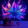 A vibrant neon cannabis leaf tapestry hangs on a dark wall above a chair.