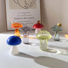 Collection de décorations en forme de champignons en verre de différentes couleurs et formes, présentées sur une surface blan