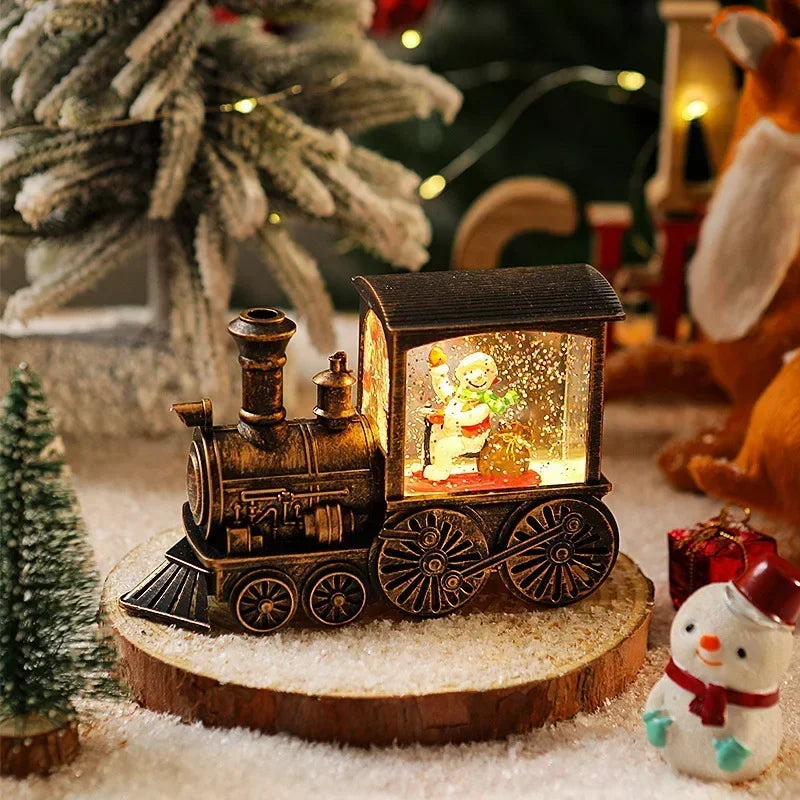 A wooden Christmas train model with an illuminated box and a crystal ball sits on a snowy surface.