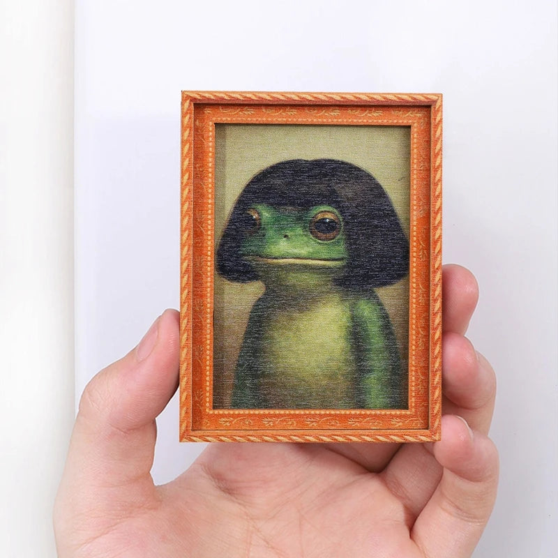 A hand holds a wooden photo frame containing an illustration of a cute green frog.