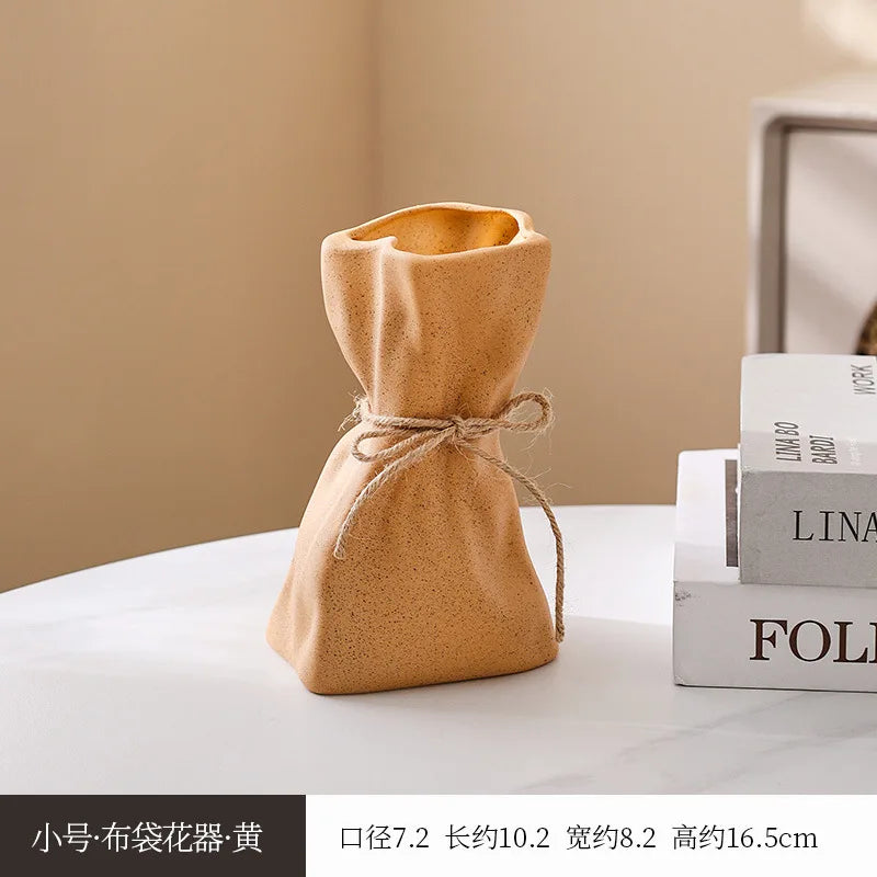 A small, light brown, fabric money bag shaped vase is displayed on a white surface.