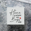 A white sign with elegant script reads Home is where my boys are with a small red heart on a textured surface.