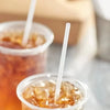 A close-up shot of two clear plastic cups filled with amber liquid and topped with white disposable straws.