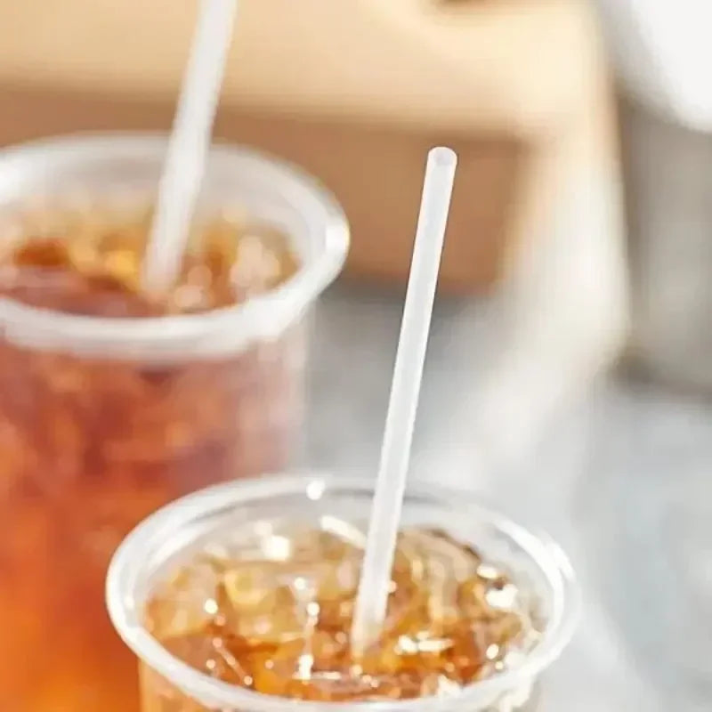 A close-up shot of two clear plastic cups filled with amber liquid and topped with white disposable straws.