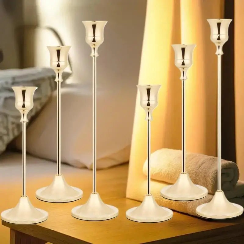 A set of three ornate vintage metal candle holders with slender stems and wide bases displayed on a wooden surface.