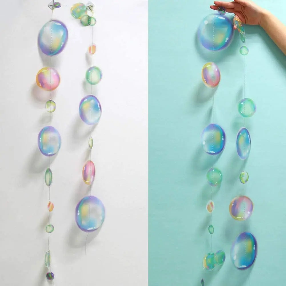 Iridescent mermaid and jellyfish party streamers hanging vertically against a light blue wall.