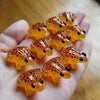 A hand holds several bright orange glow-in-the-dark resin frog ornaments.