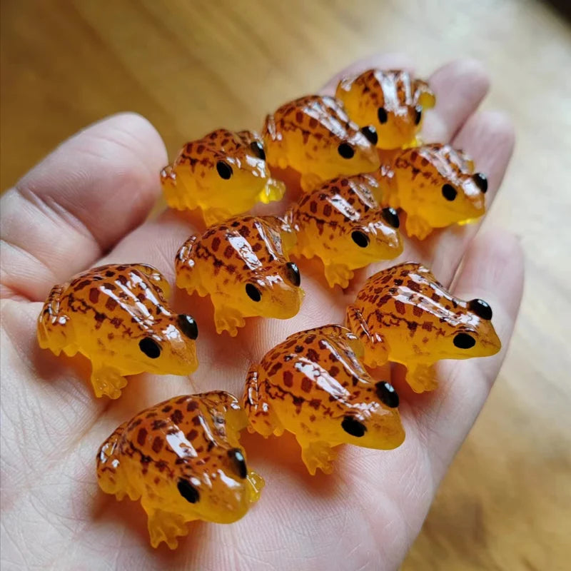 A hand holds several bright orange glow-in-the-dark resin frog ornaments.
