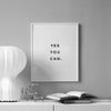 A framed motivational quote print on a gray wall with the text YES YOU CAN.