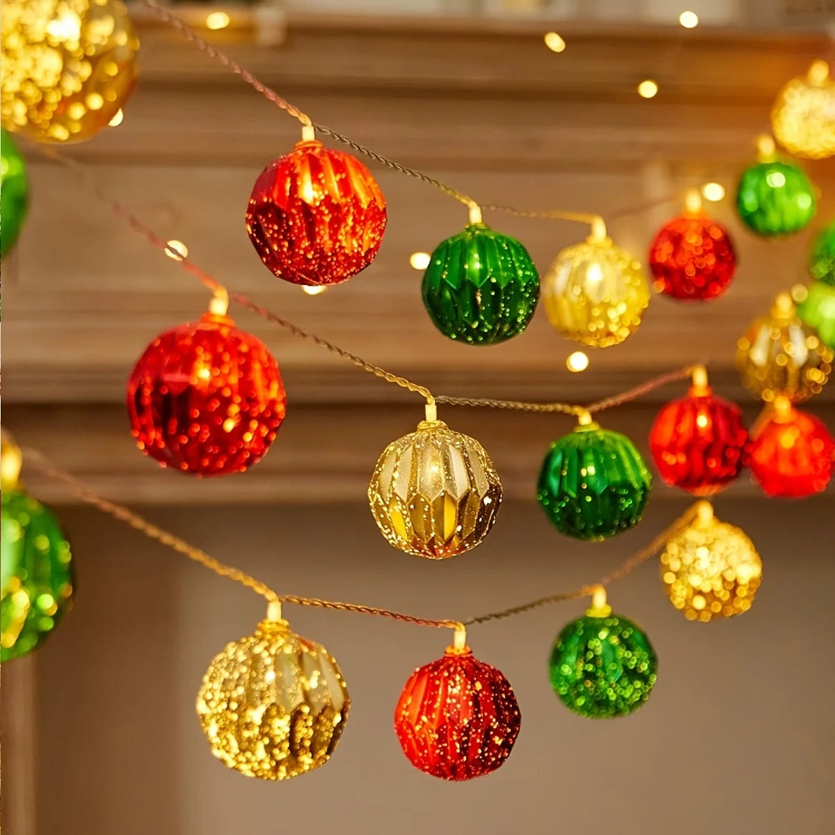 A string of festive LED fairy lights featuring round ornaments in red, green, and gold hanging against a wooden background.