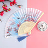 A vintage silk folding hand fan with blue and red floral designs is displayed on a pink background.