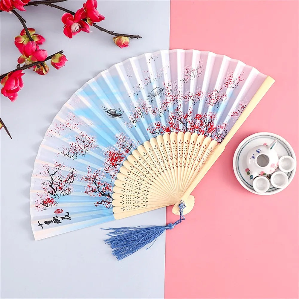 A vintage silk folding hand fan with blue and red floral designs is displayed on a pink background.