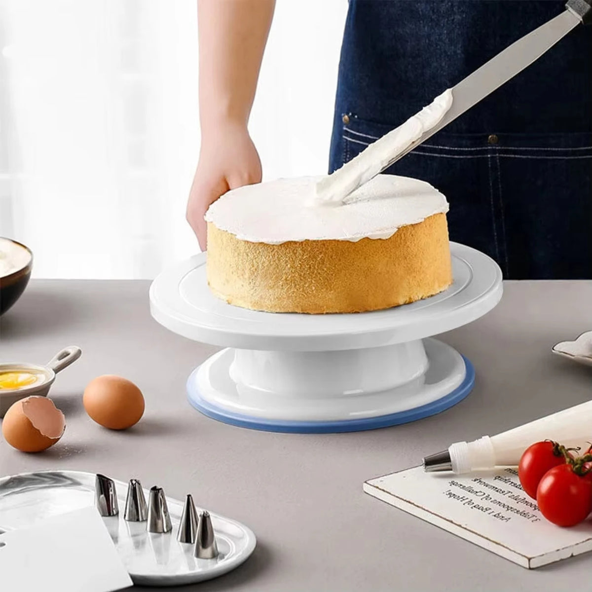 Eine Hand benutzt einen Metallspatel, um einen runden Kuchen auf einem weißen Tortenständer zu dekorieren.