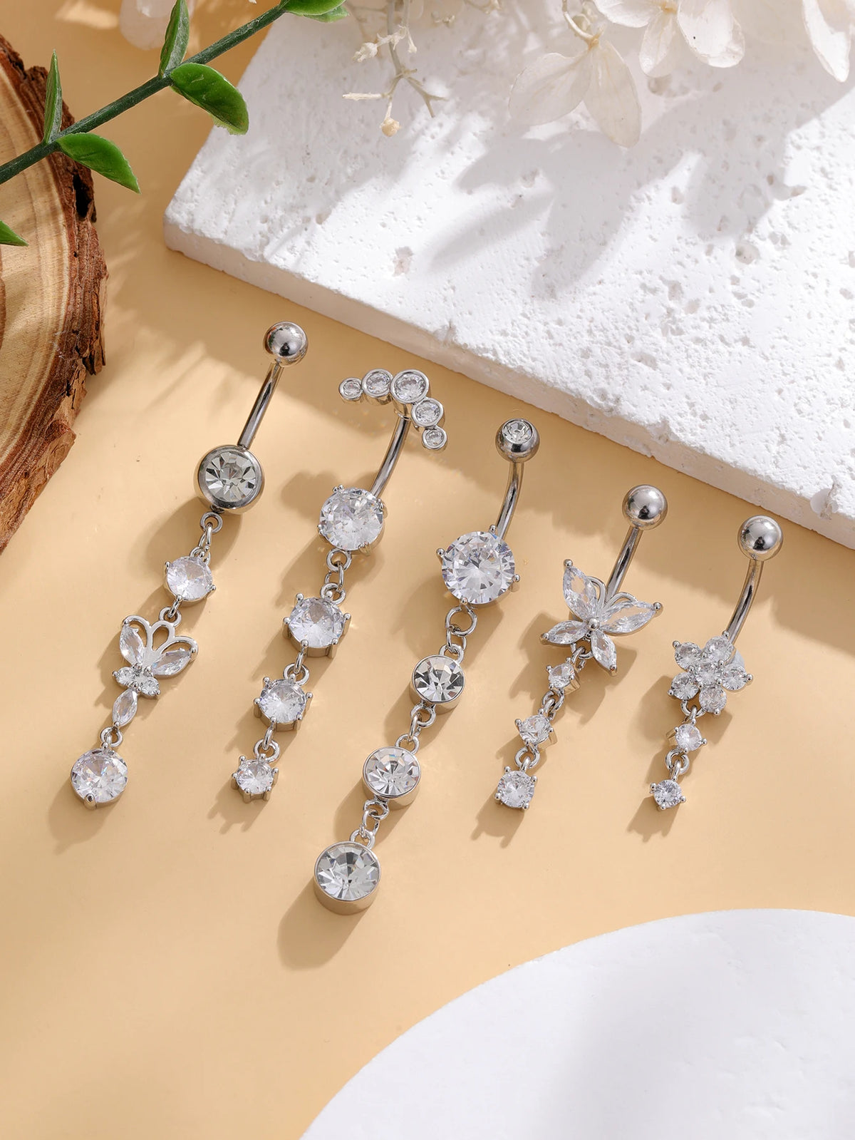 A set of five gold tone butterfly and flower belly rings displayed on a light background with natural elements.