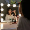 A person is looking into a dimmable LED vanity mirror while applying makeup.