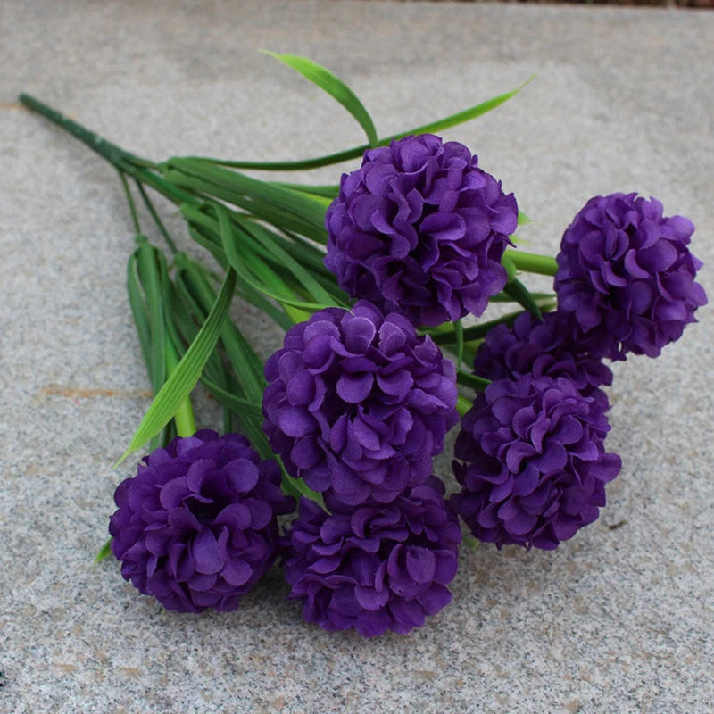 Un bouquet de fleurs artificielles d'hydrangea violettes sur une surface grise.