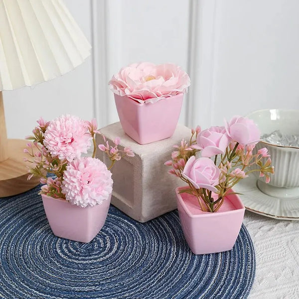 A set of three pink artificial roses in potted containers displayed on a blue textured mat.
