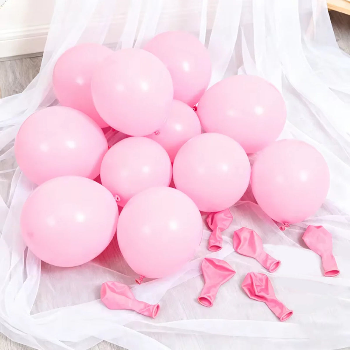 A collection of pink latex balloons and pink ribbon streamers laid out on white fabric.