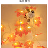 An autumn leaf garland with orange and red leaves illuminated by warm LED lights for fall decoration.