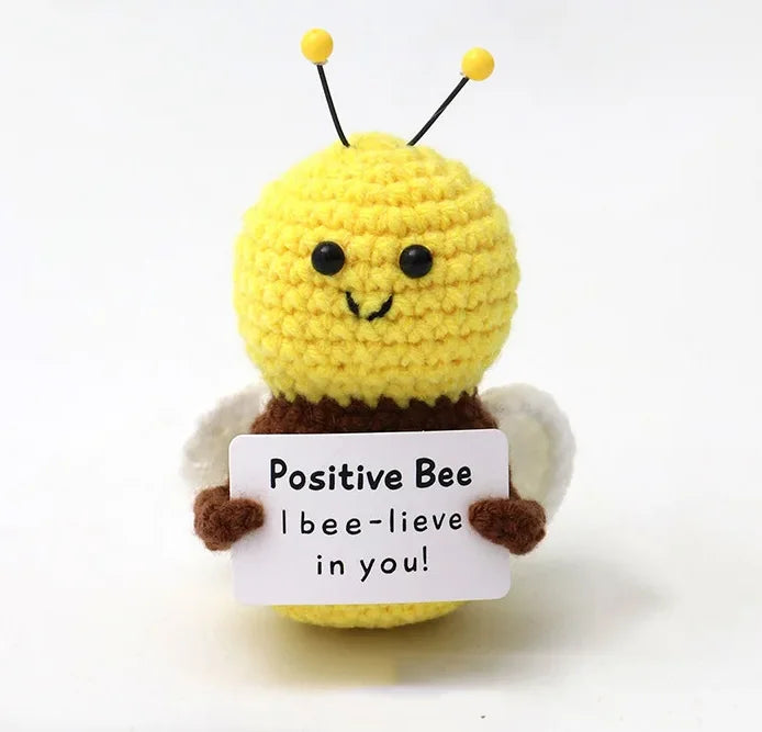 A yellow knitted plush bee with black antennae and a sign that reads Positive Bee I bee-believe in you