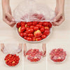 Hands holding a clear reusable elastic food cover over a bowl of fresh red tomatoes.