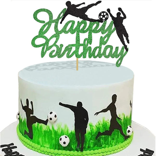 A white birthday cake decorated with green grass and black silhouettes of people playing football, topped with a green glitte
